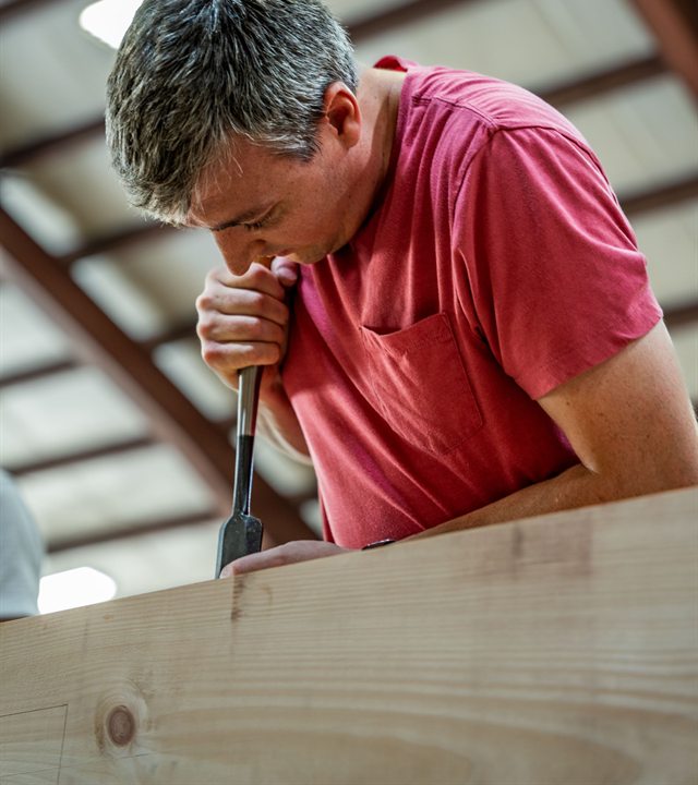 Joseph K. Lane cutting a mortise with a chisel while framing a timber shelter.